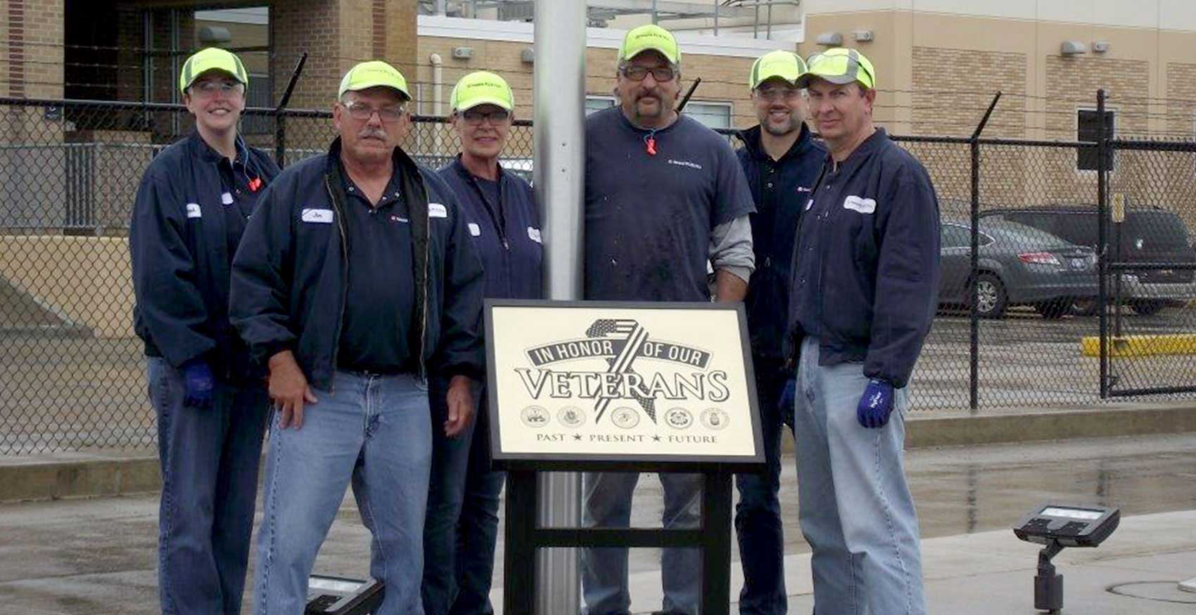Factory associates standing in front of Honoring Our Veterans sign